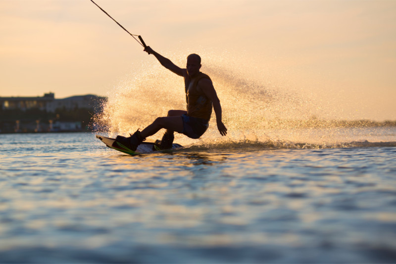 Persona practicando wakeboard al atardecer detrás de una embarcación